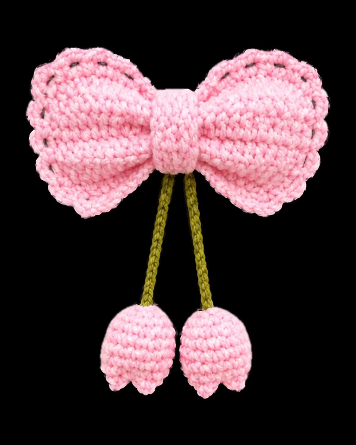 Baby-pink crochet bow hair clip with two olive-green chain cords ending in small pink crochet tulip buds, on a cream background