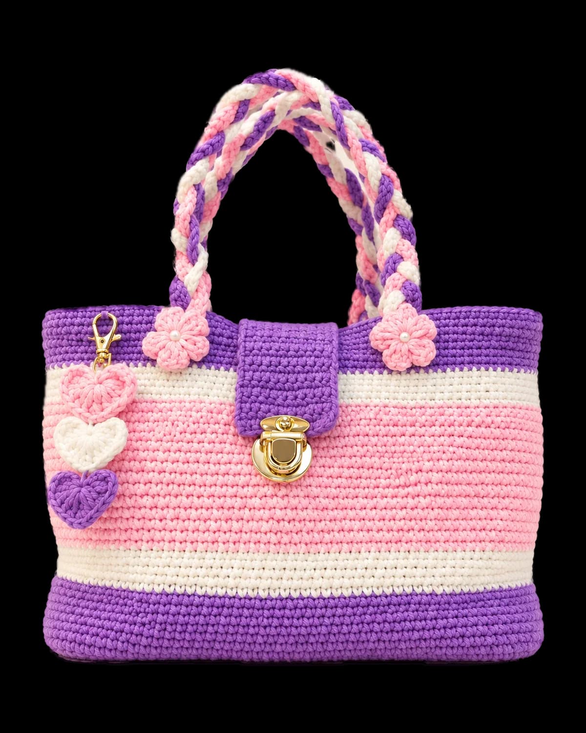 Crochet handbag striped in lilac, white and soft pink, with braided handles, pearl-centred pink flowers, a gold-tone push-lock clasp and a three-heart charm, on a cream background
