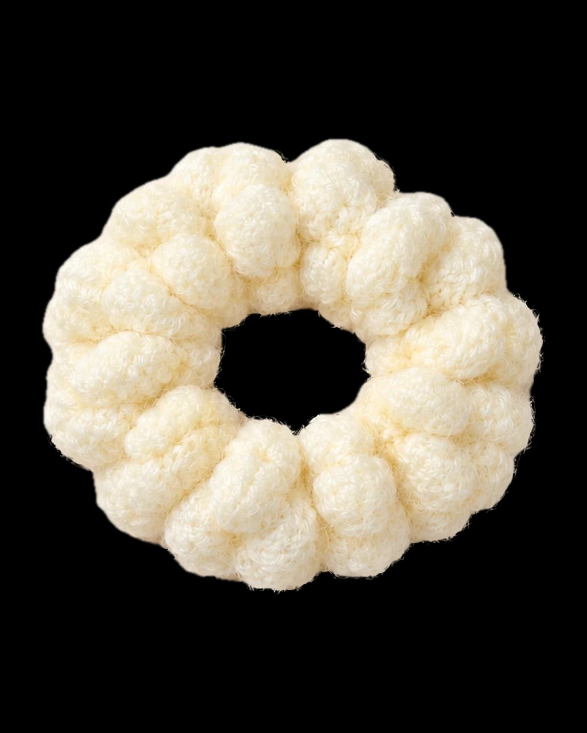 Cream crochet scrunchie made of plump puff stitches, lying flat on a warm cream background