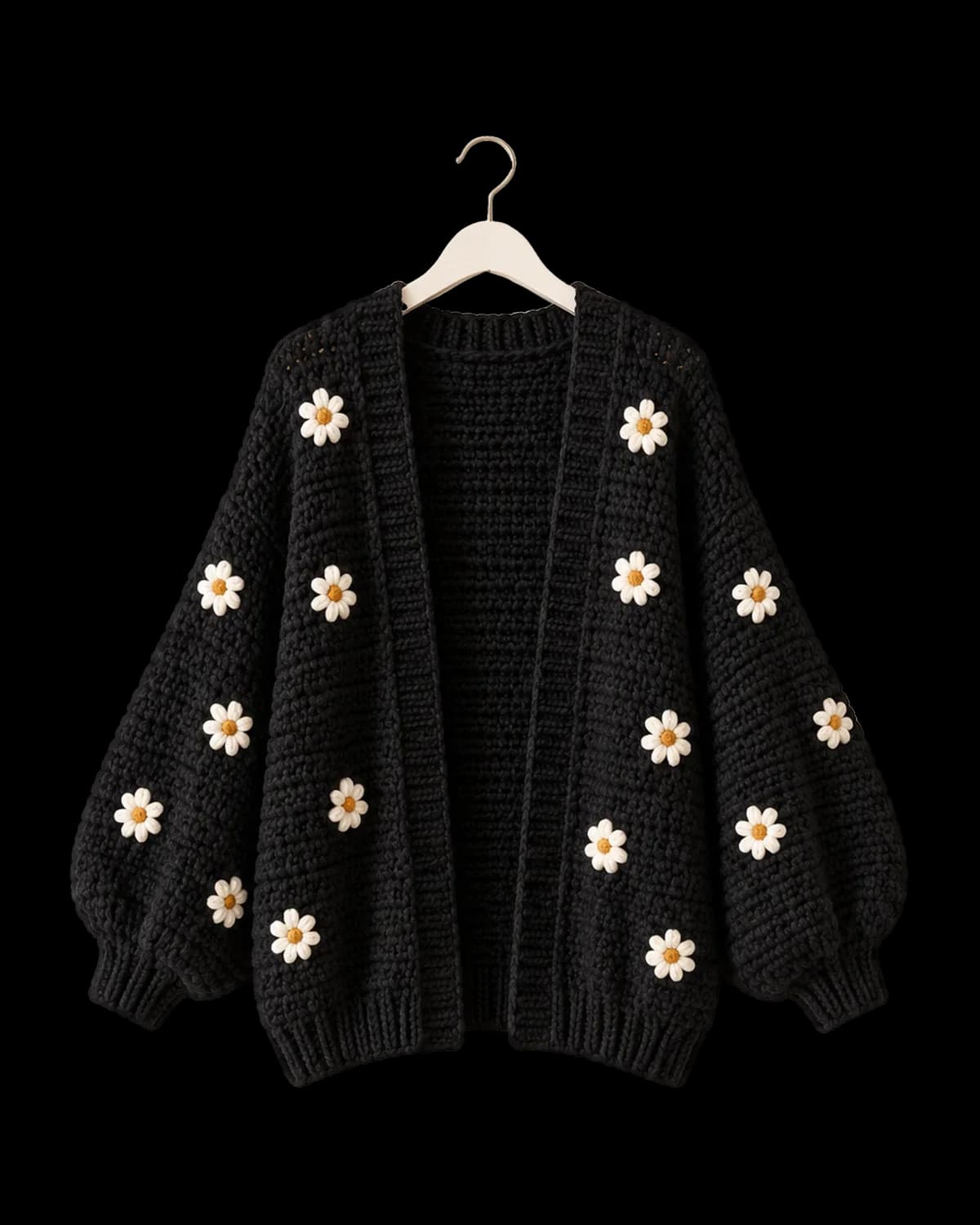 Black oversized crochet cardigan with white puff-stitch daisies and balloon sleeves on a cream hanger