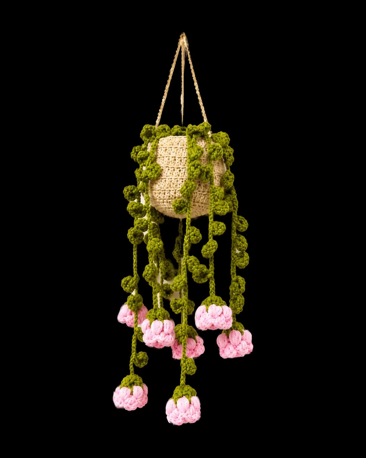 Crochet hanging planter with a beige pot, trailing green leaf vines and pink rosebuds on a cream background