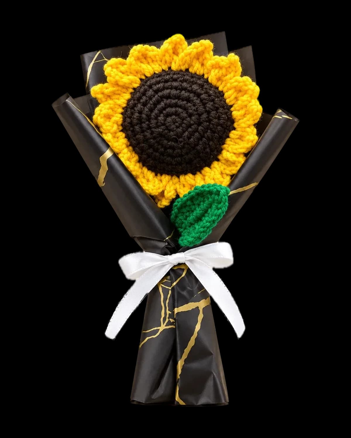 Hand-crocheted sunflower bouquet with a green leaf, wrapped in black and gold paper and tied with a white satin ribbon